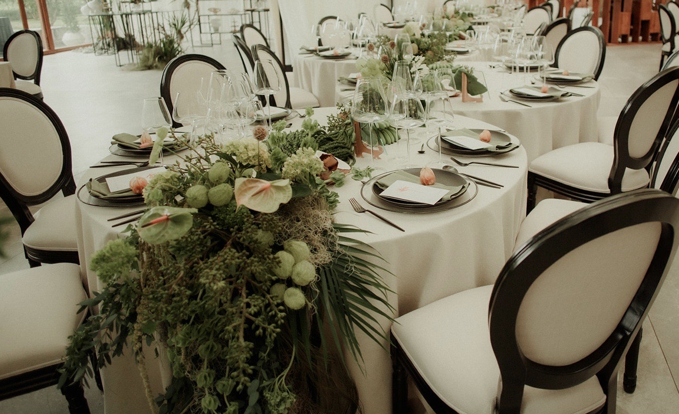 Mesa larga decorada con follaje y vajilla elegante