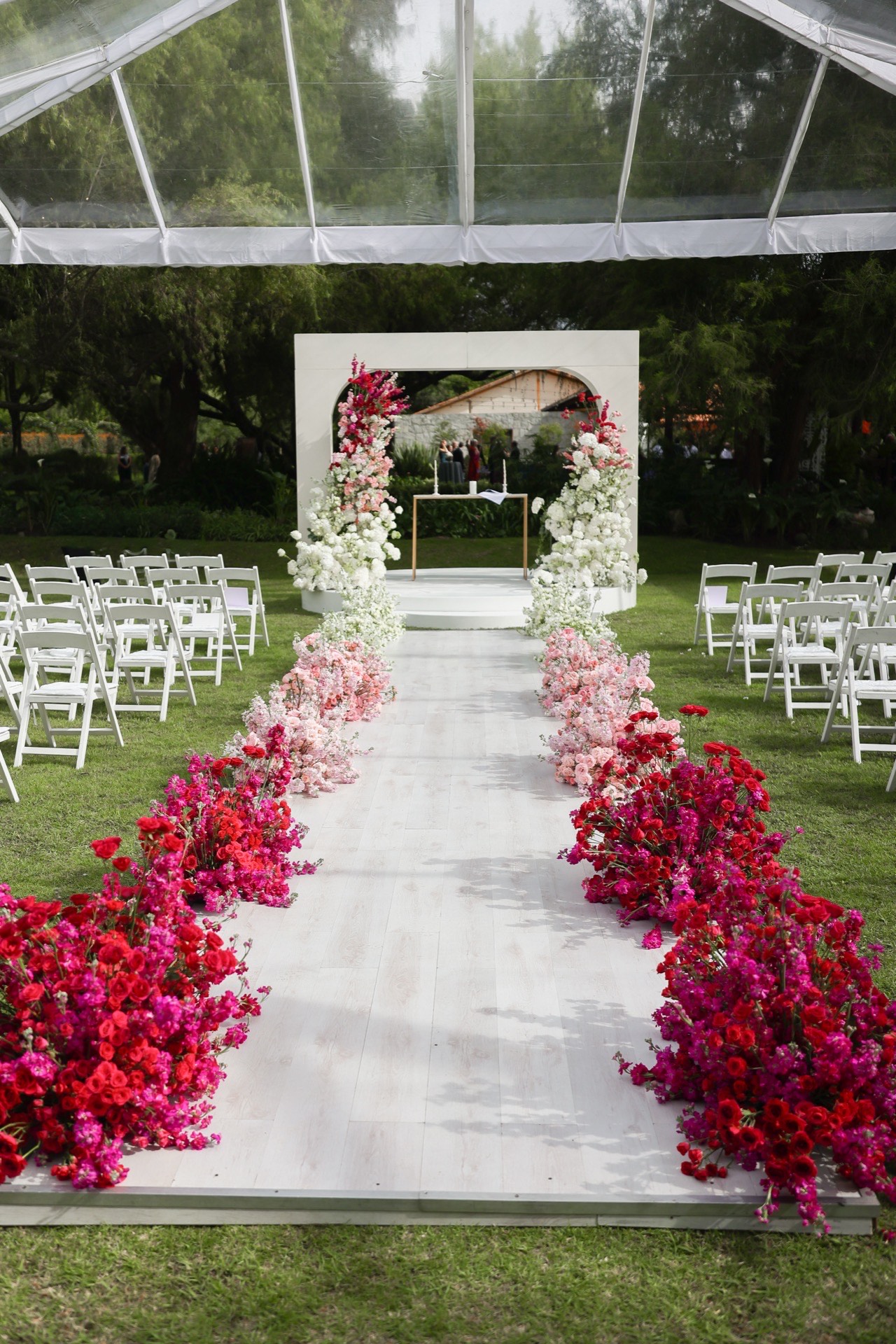 Pasillo de ceremonia con pétalos rojos y arco floral