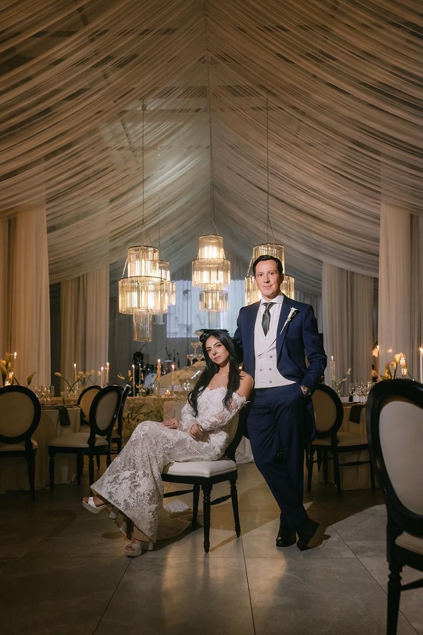 Novios sentados en la recepción bajo carpa iluminada