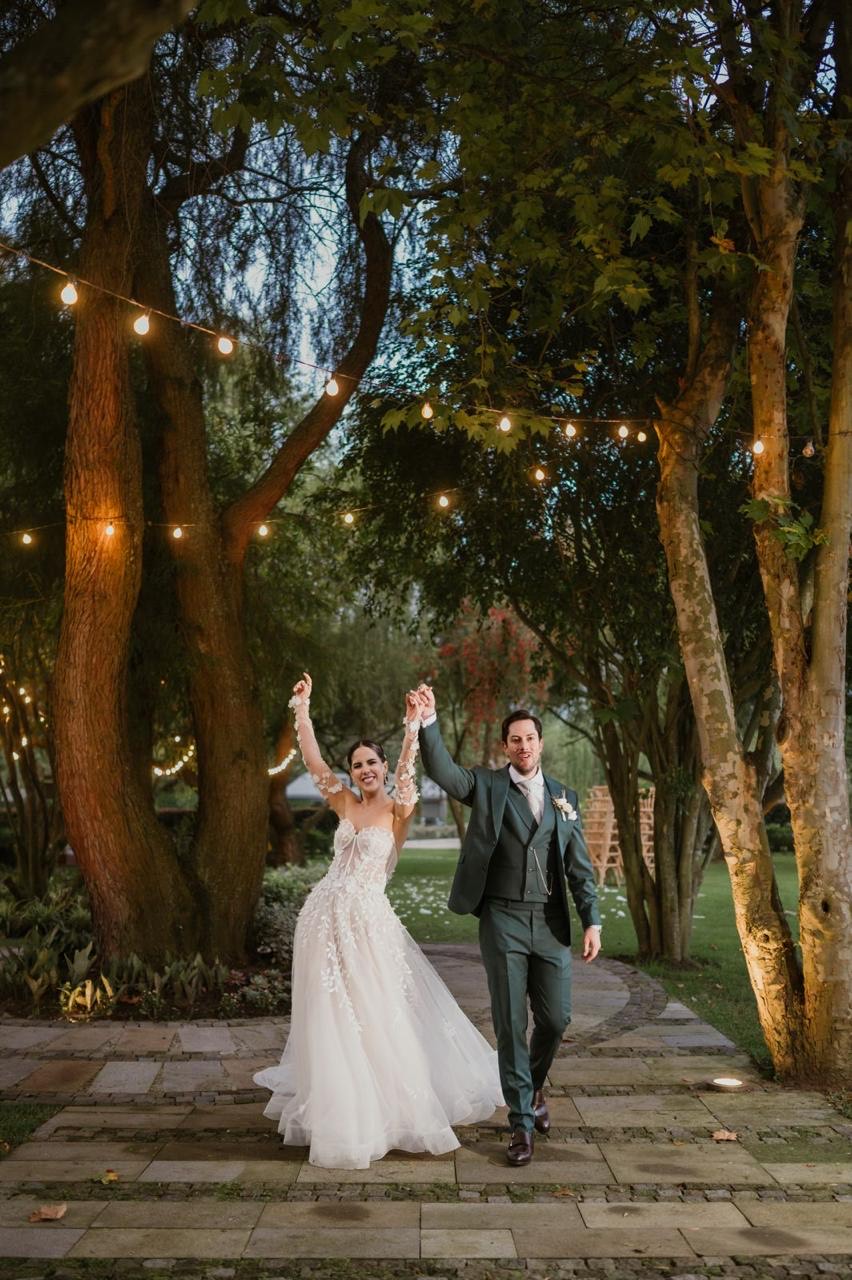 Novios celebrando tomados de la mano bajo luces cálidas