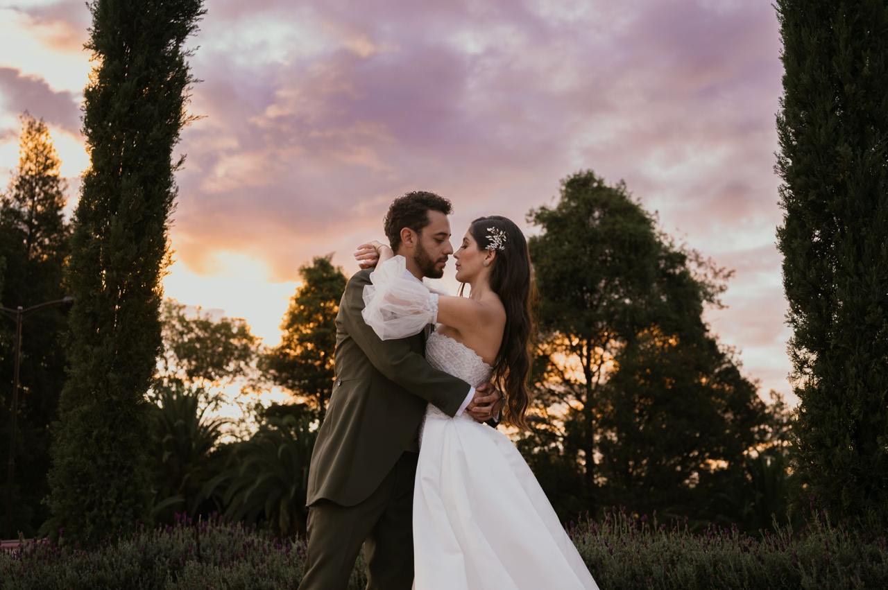 Novios abrazados frente a un atardecer con nubes rosadas
