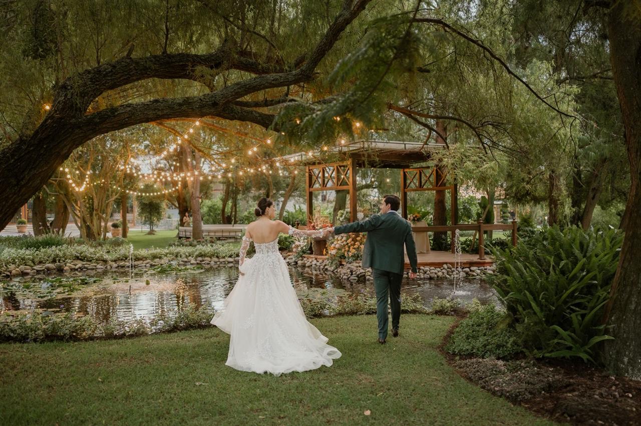 Novios caminando hacia el mirador iluminado junto al estanque